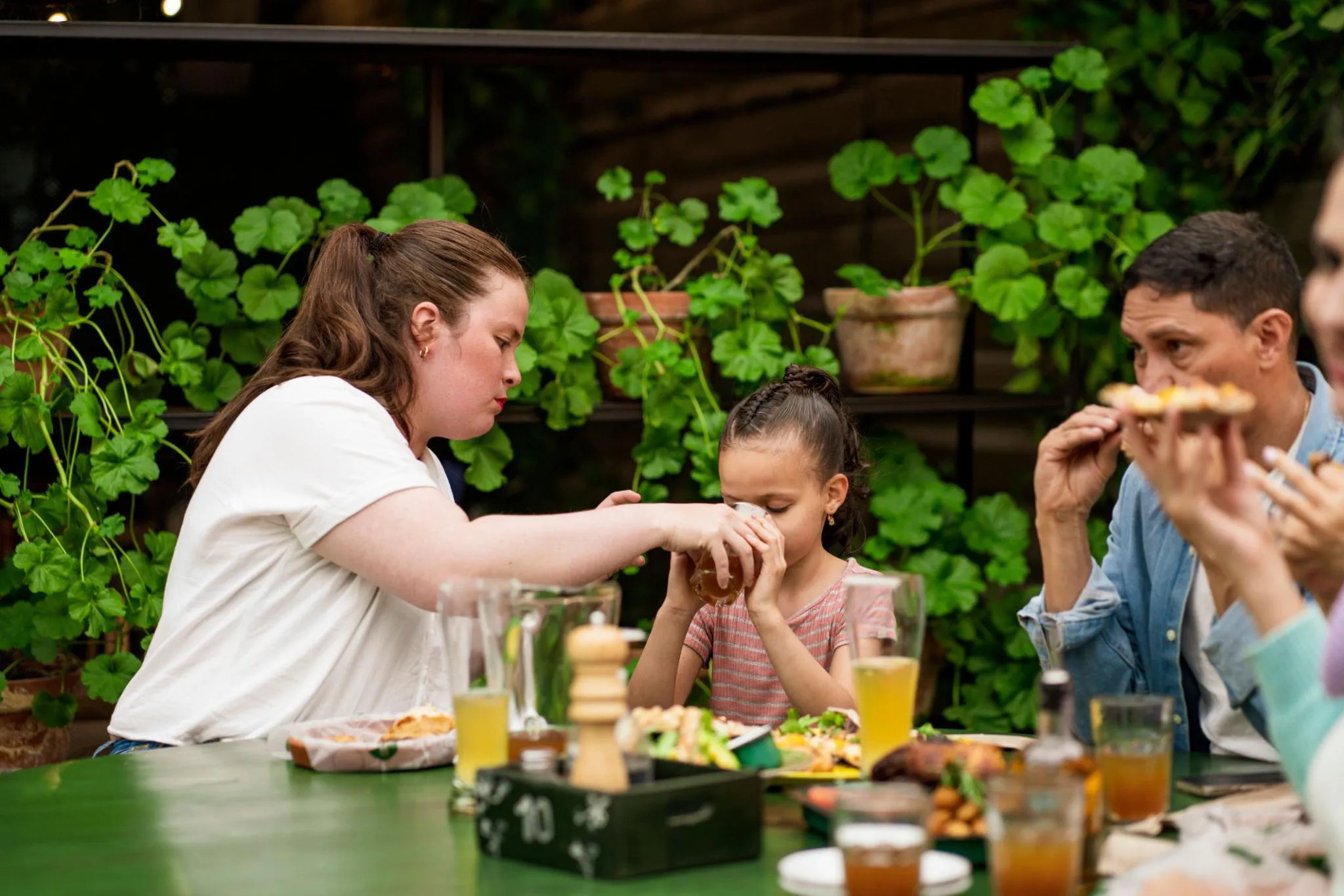 A family enjoying a meal together at an outdoor dining table surrounded by green plants