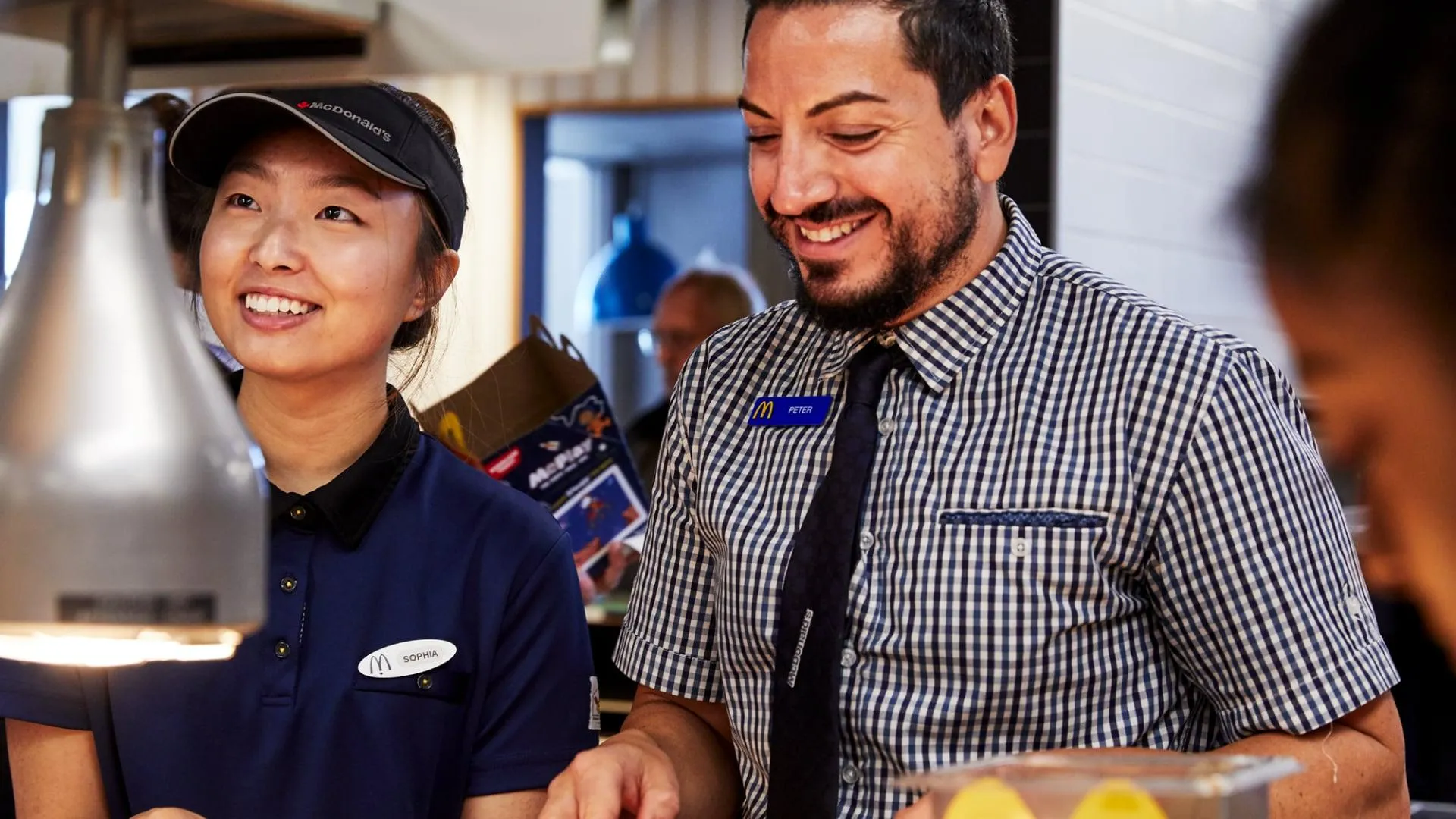 A male McDonald's manager and a female crew member laughing together while working A male McDonald's manager and a female crew member laughing together while working