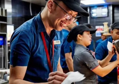 A smiling kitchen employee wearing glasses working alongside team members